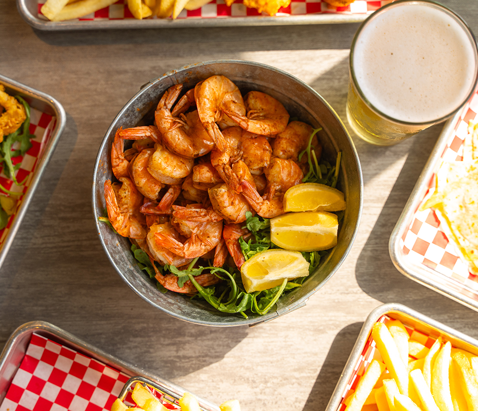 a bowl of shrimp and lemons next to a glass of beer