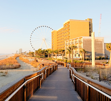 a boardwalk leading to a beach with a ferris wheel and buildings