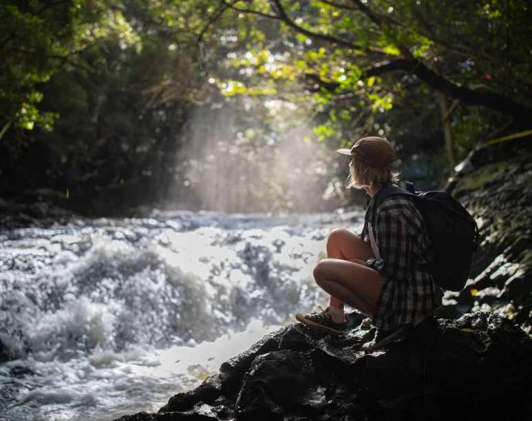 a woman sitting on a rock near a river
