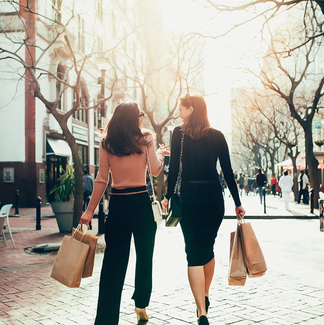 two women walking down a sidewalk with shopping bags