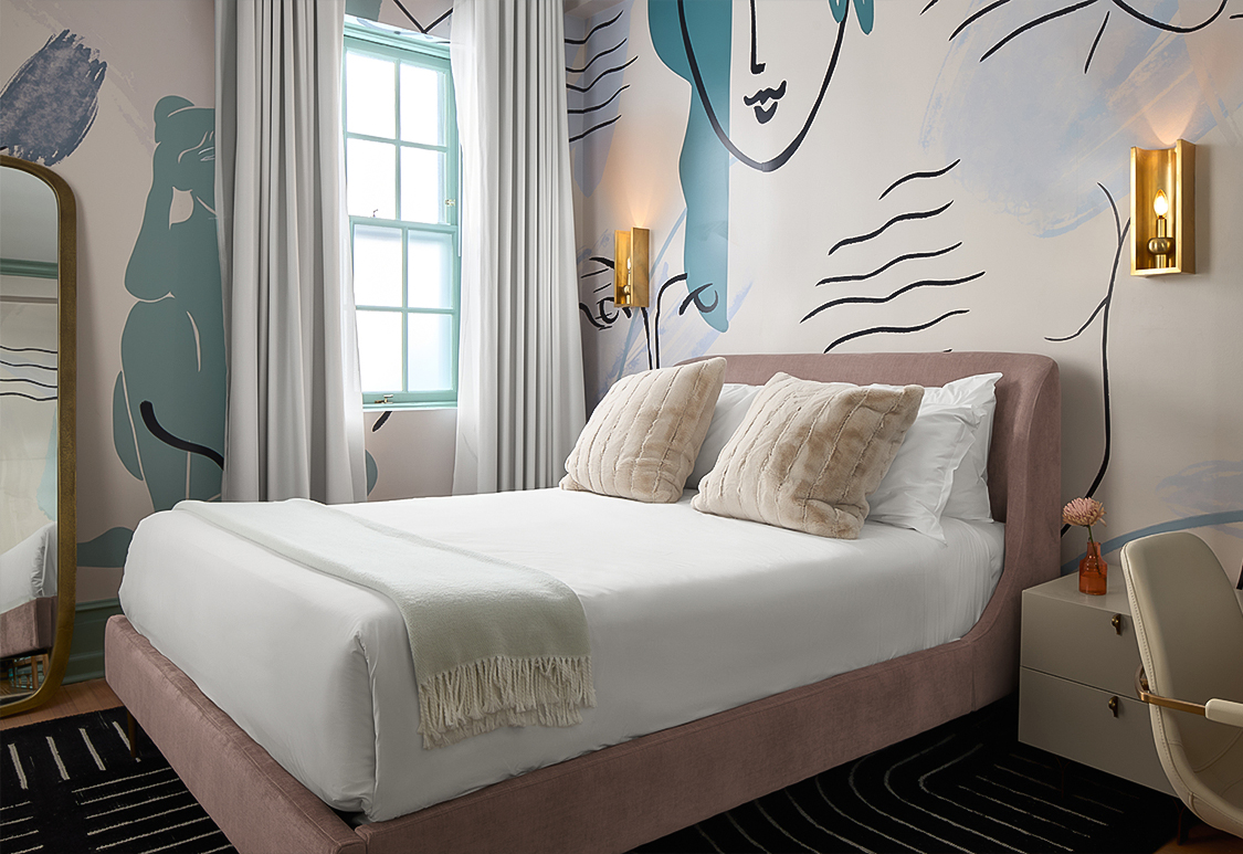 a bed with pillows and a wall with a painting on the wall