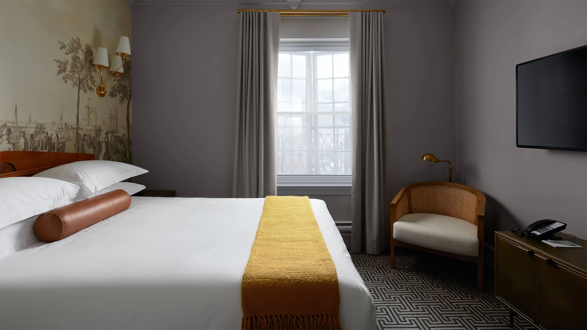 A hotel room with a large bed, chair, TV, and window.