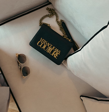 A close-up view of a bed with a Versace bag and sunglasses on it.