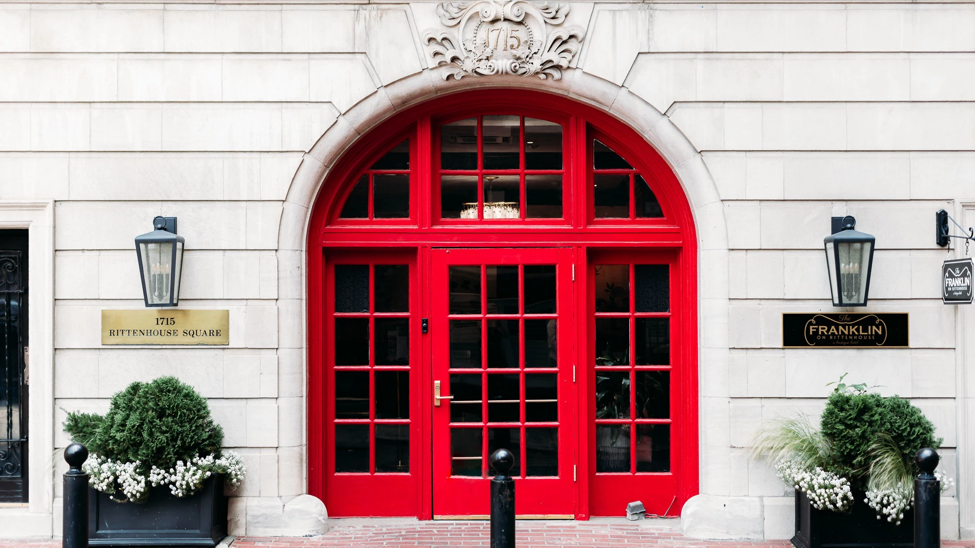 A red arched doorway with a stone facade and planters on either side.