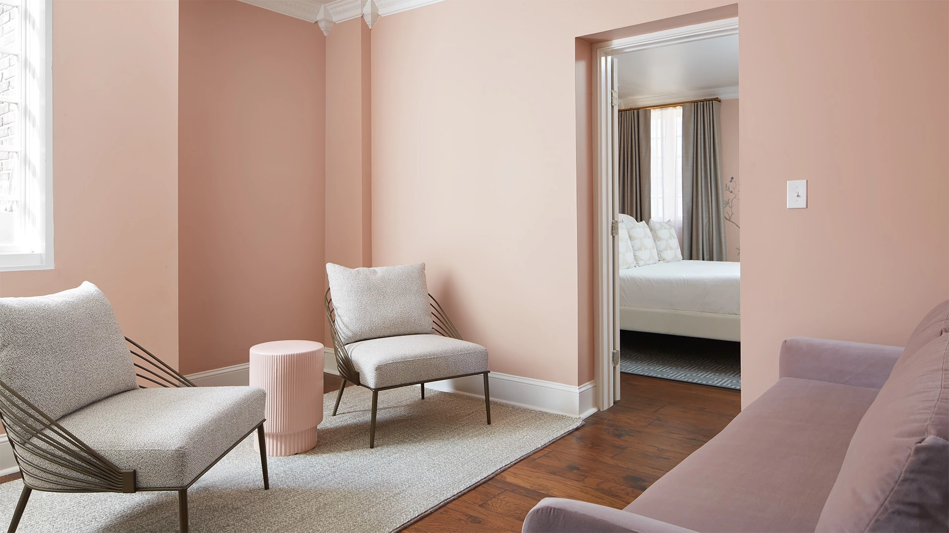 A room with pink walls, a wood floor, and a doorway leading to a bed.