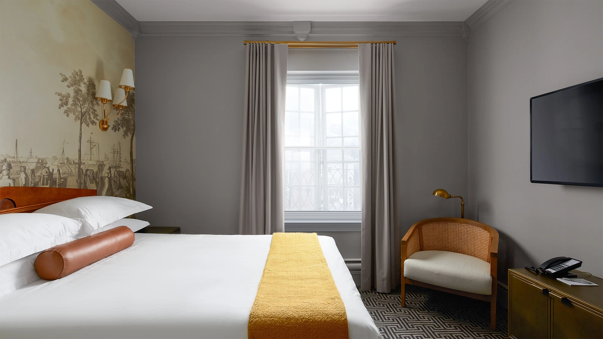 A hotel room with a bed, chair, TV, and window