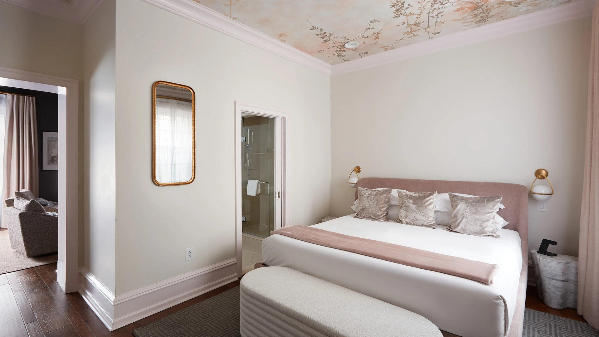 A wide view of a hotel room with a bed, bench, and doorway to another room