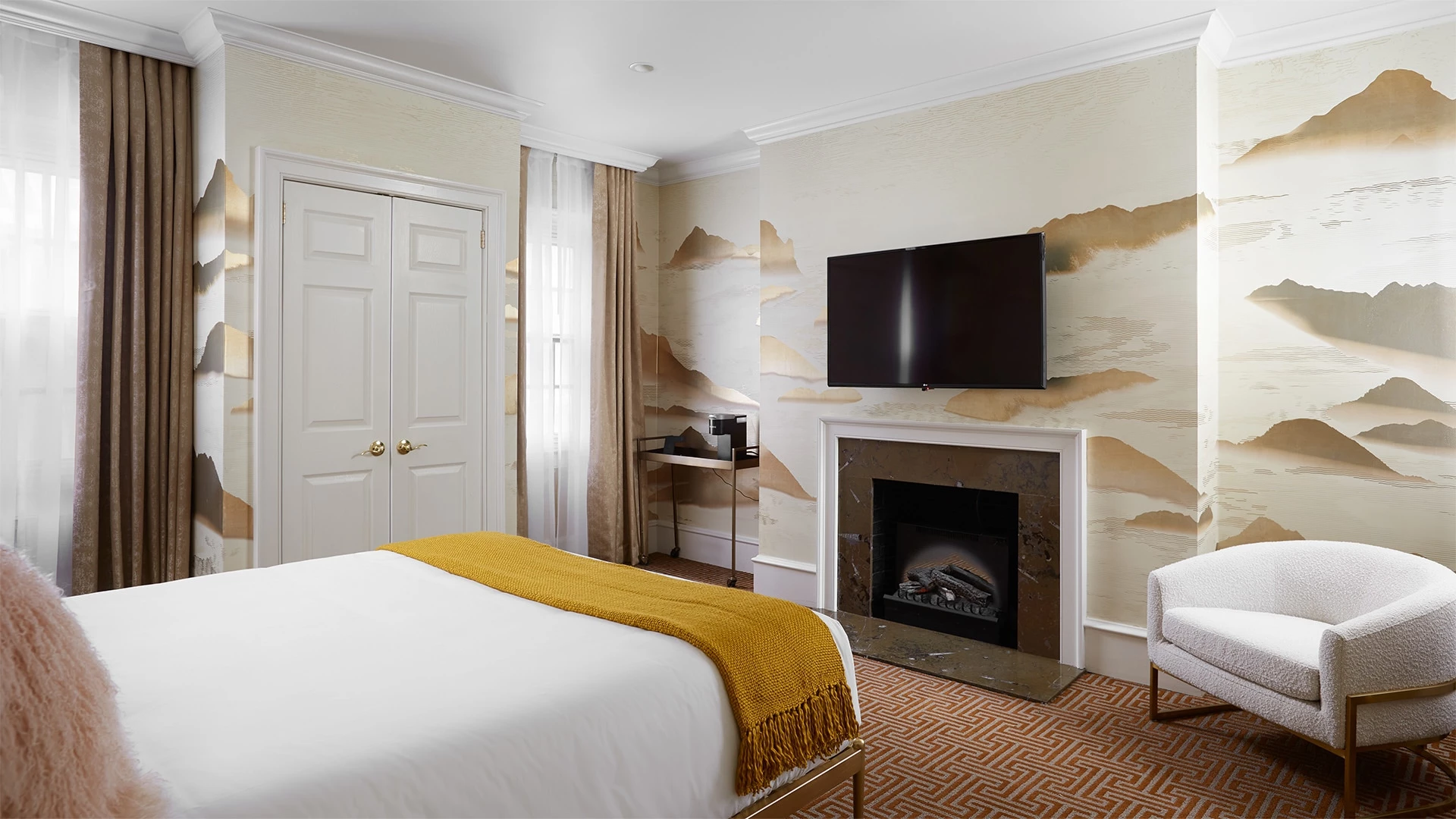 A hotel room with a bed, fireplace, chair, and TV