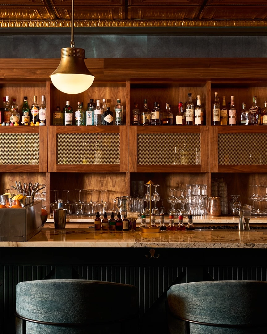 a bar with two stools, a counter, and shelves of bottles and glasses