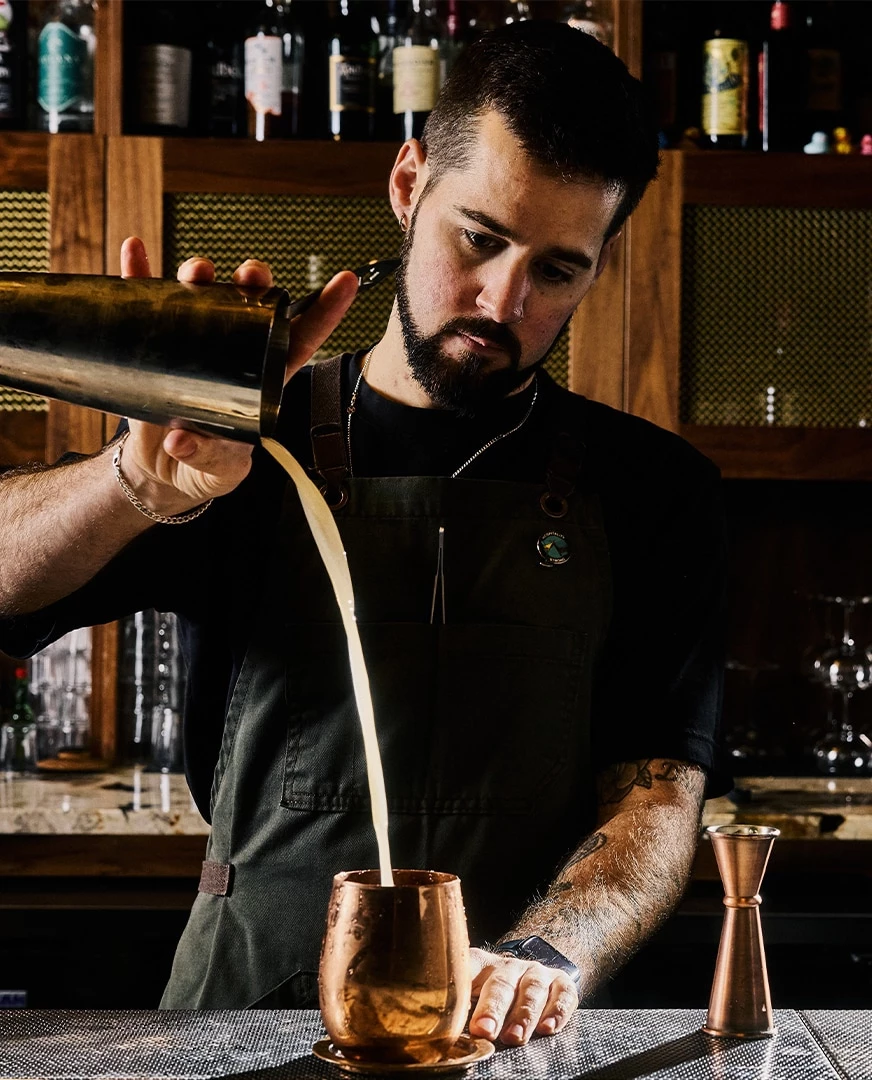 A bartender pouring a drink into a copper mug.