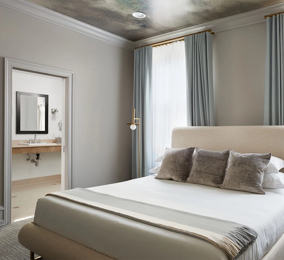 A wide view of a hotel room with a large bed, a window with curtains, and an open doorway to a bathroom.