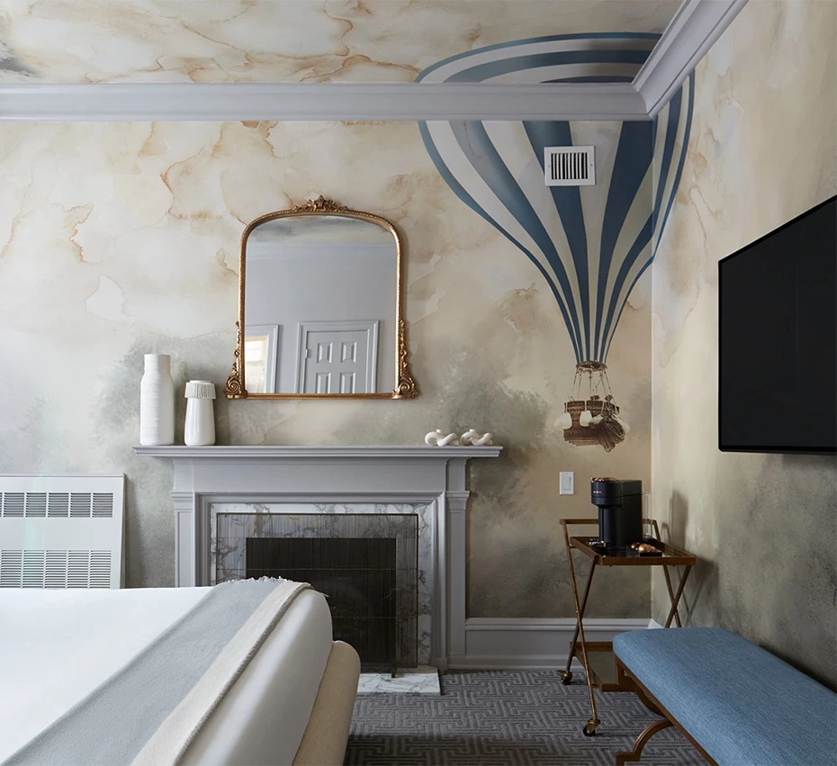 A luxurious hotel room with a hot air balloon mural, marble wall, fireplace, and modern amenities.