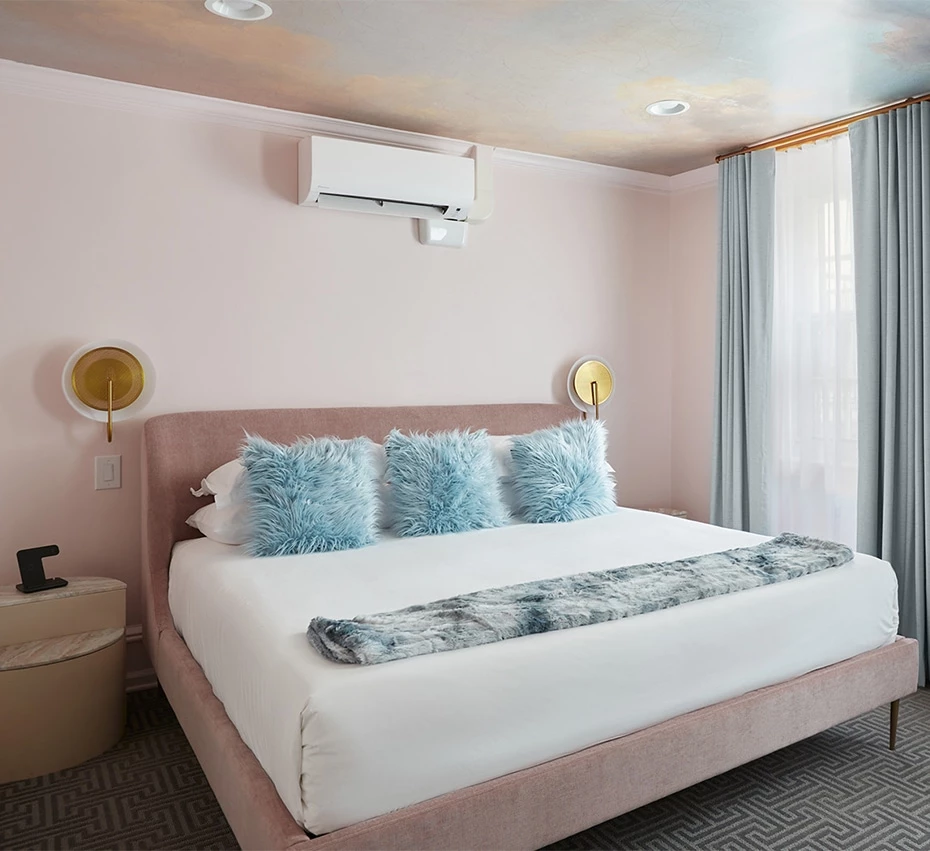 A neatly made bed with white linens and blue pillows in a room with pink walls and a decorative ceiling.