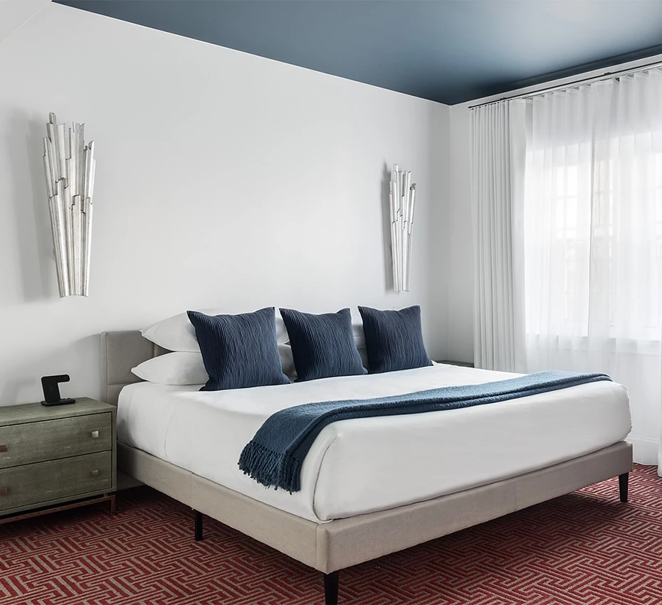 A wide view of a hotel room with a bed, nightstand, and window.