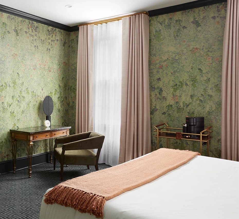 A wide view of a hotel room with a king bed, floral wallpaper, and a desk with chair.