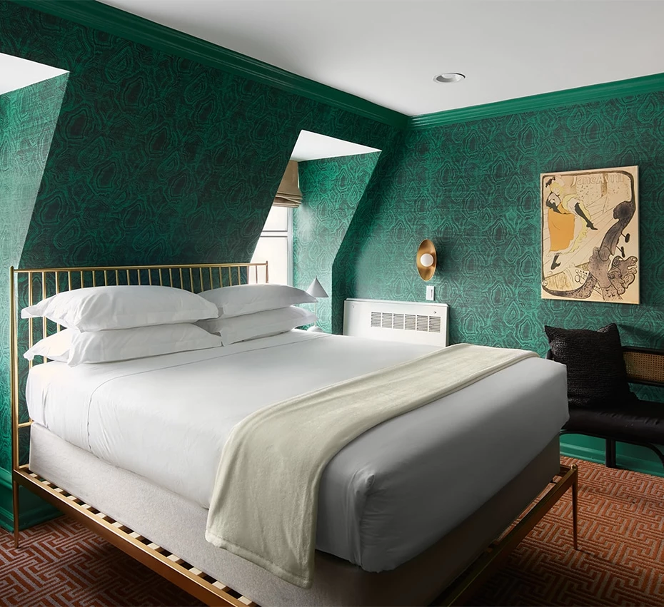 A large bed with white linens and a green wall with patterned wallpaper.