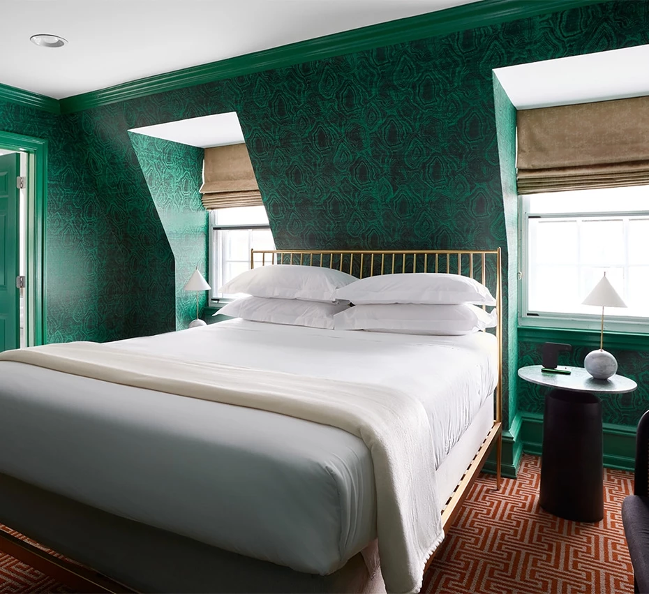 A wide view of a hotel room with a king-sized bed, green wallpaper, and a gold headboard.