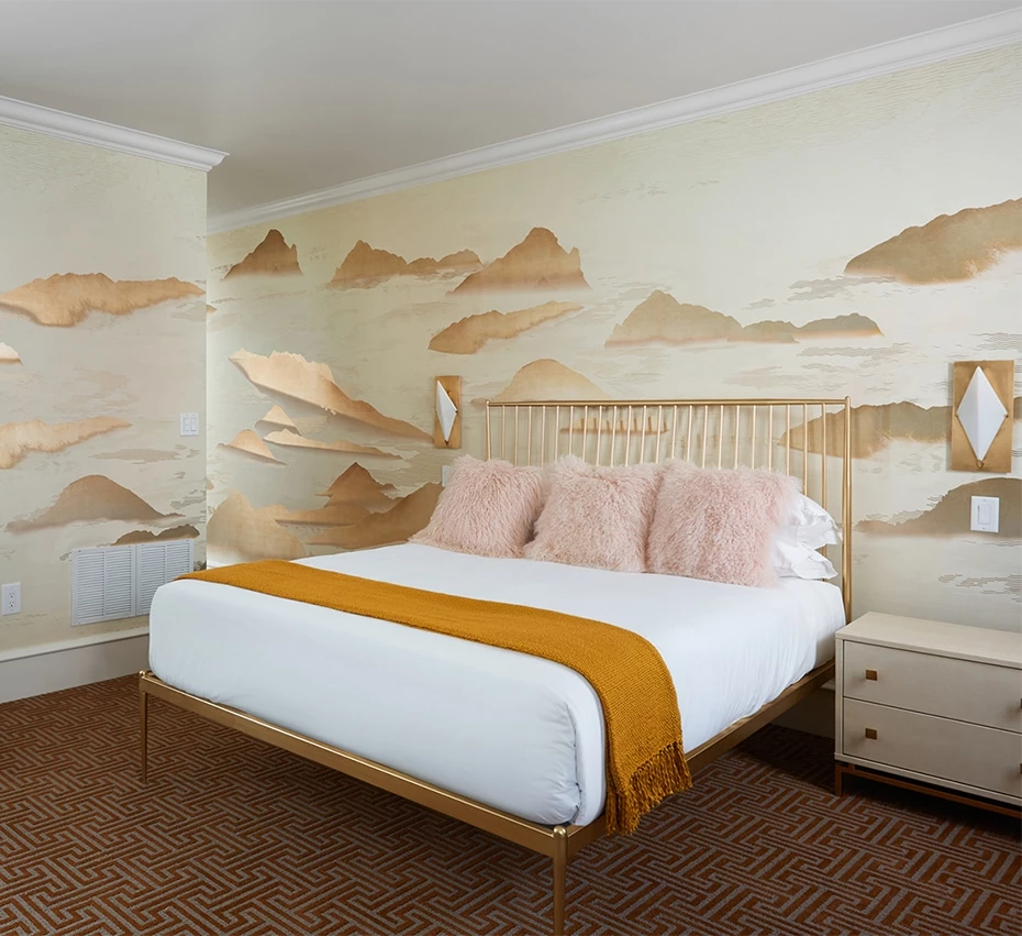 A hotel room with a bed, nightstand, and decorative mural on the wall.