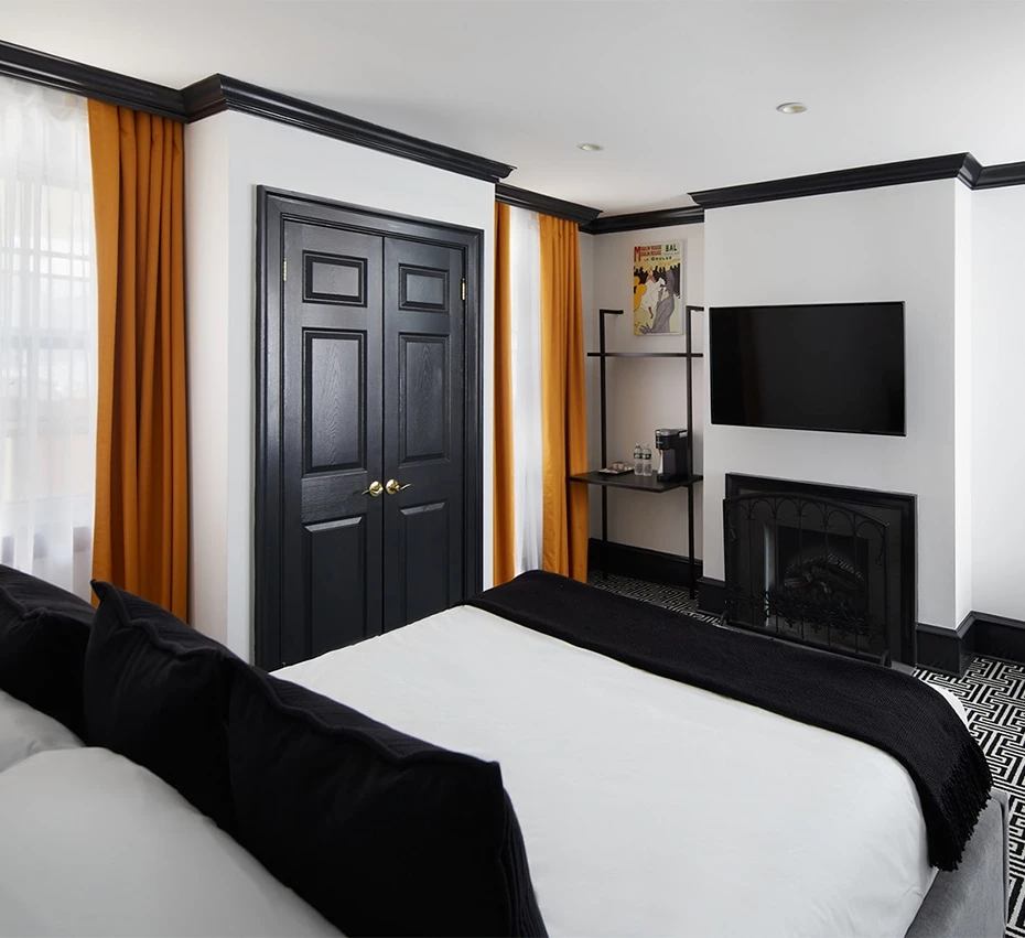A hotel room with a bed, fireplace, TV, and door