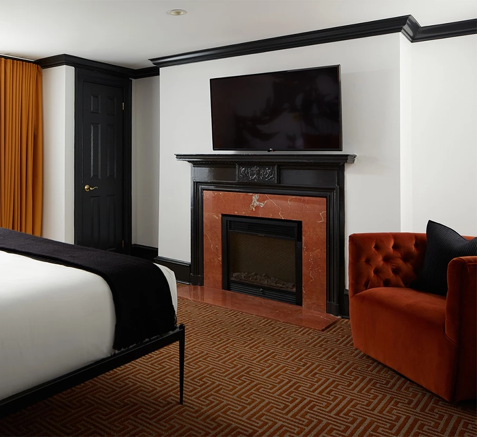 A hotel room with a bed, fireplace, chair, and TV