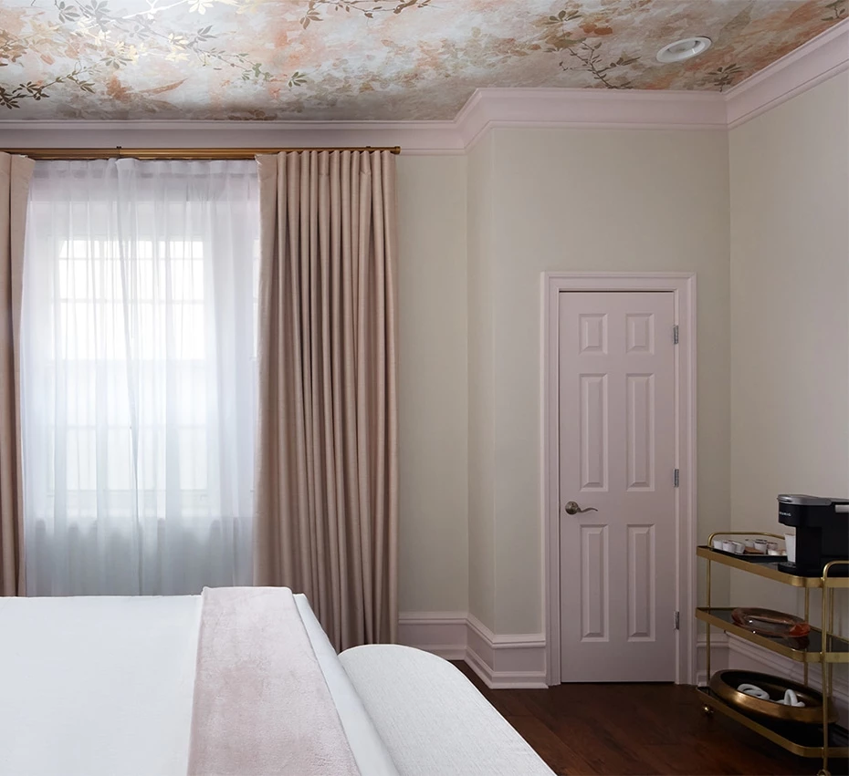 A luxurious hotel room with a white bed, floral ceiling, and gold accents.
