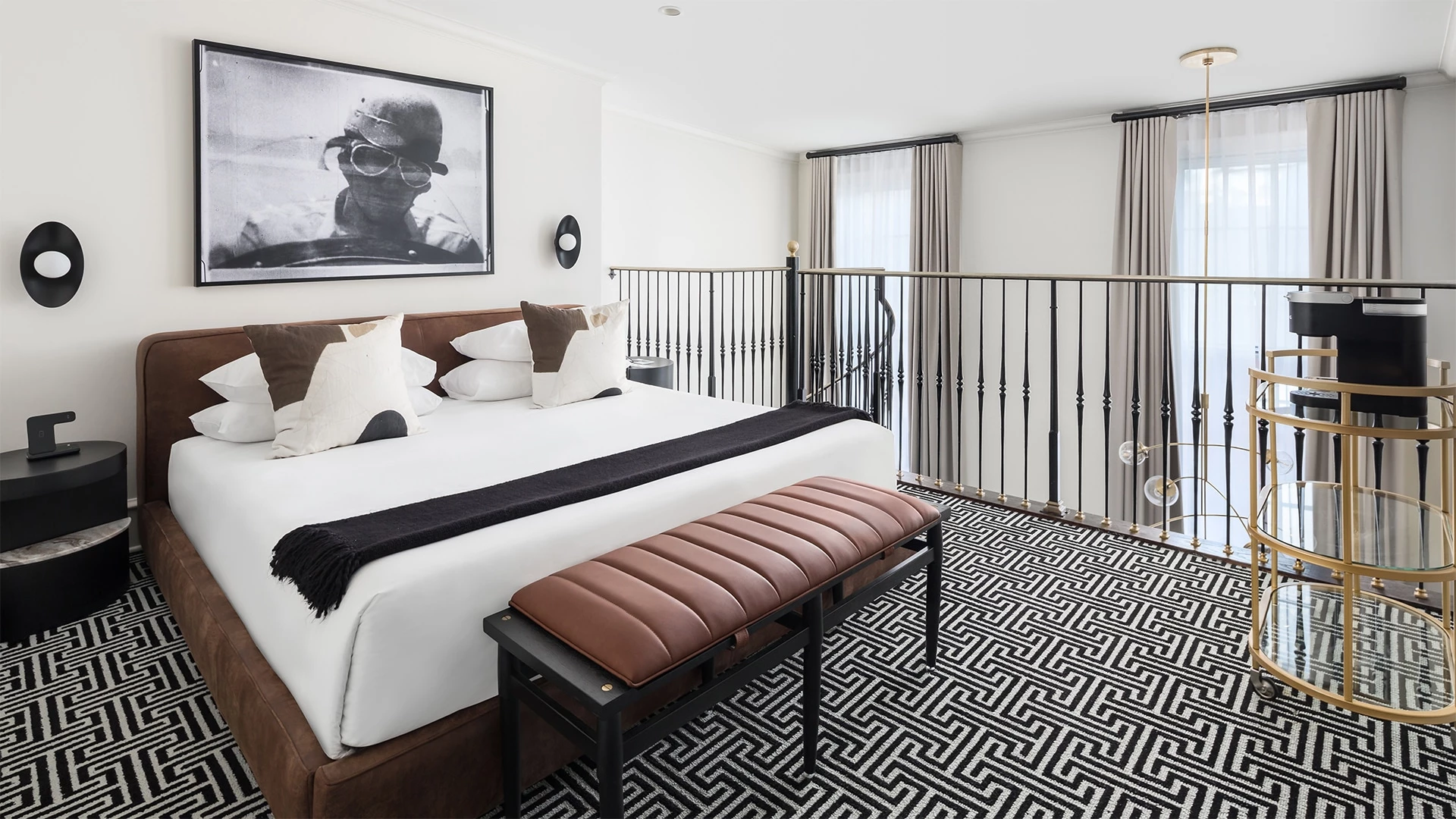 A wide view of a hotel room with a large bed, nightstand, and balcony railing.
