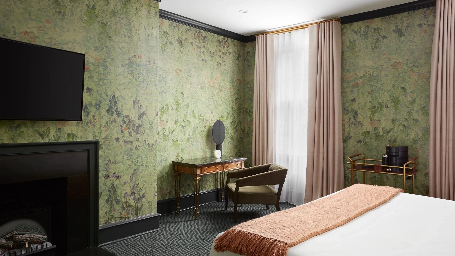 A hotel room with a bed, desk, chair, fireplace, and TV