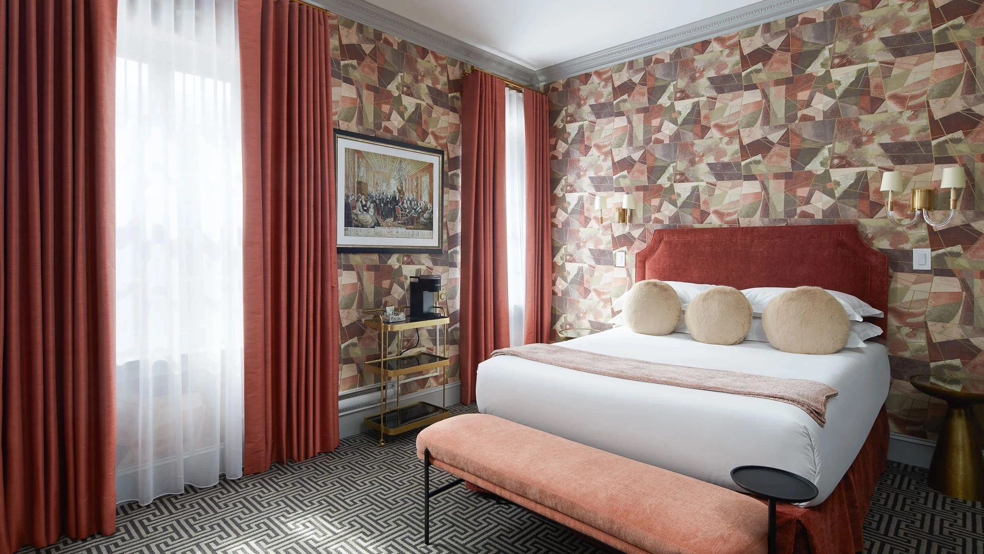 A hotel room with a large bed, red headboard, and patterned wallpaper.