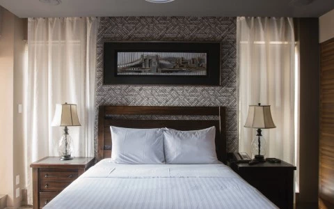 A neatly made bed with white bedding and pillows, flanked by two nightstands with lamps, against a patterned wallpaper backdrop.