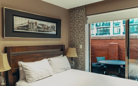 A hotel room with a large bed, two nightstands with lamps, and a sliding glass door leading to a balcony.