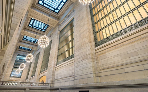 A high-ceilinged lobby with large windows, chandeliers, and ornate stone work.