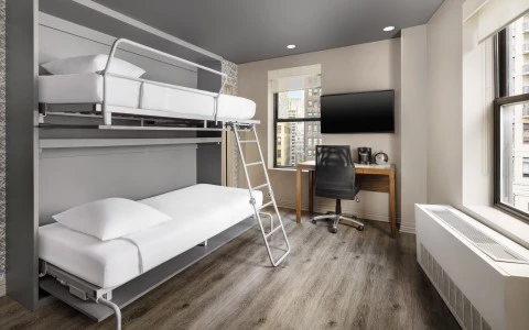 A compact hotel room with bunk beds, a desk, TV, and window