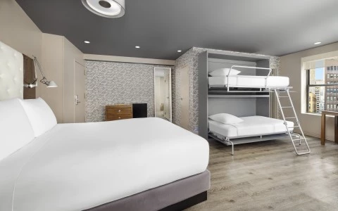 A wide room with a large bed, bunk beds, and a city view.