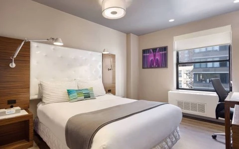 A hotel room with a bed, desk, and window