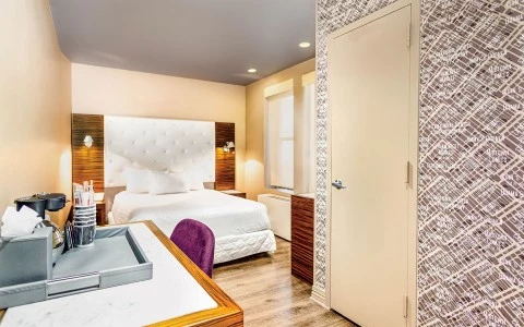 A wide view of a hotel room with a bed, desk, and door.