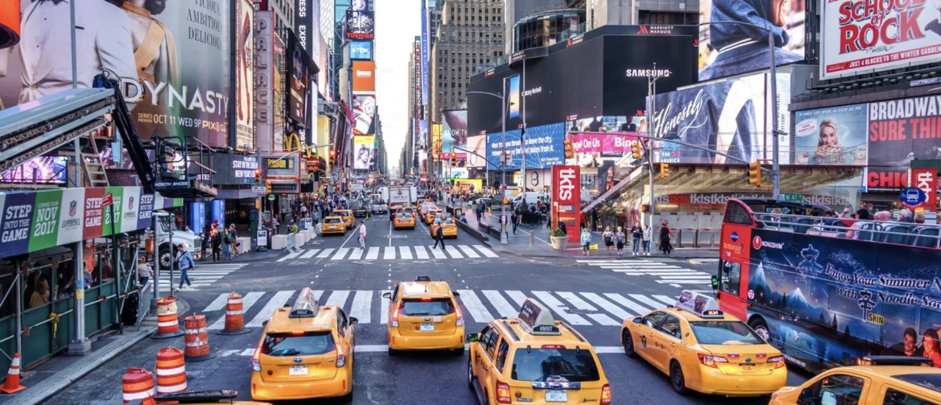 A busy street in New York City with yellow taxis and large billboards