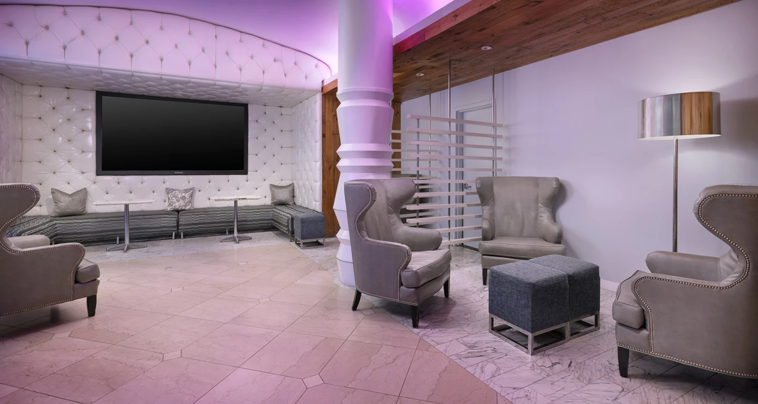 A luxurious lobby with a large screen, tufted wall, and gray chairs.