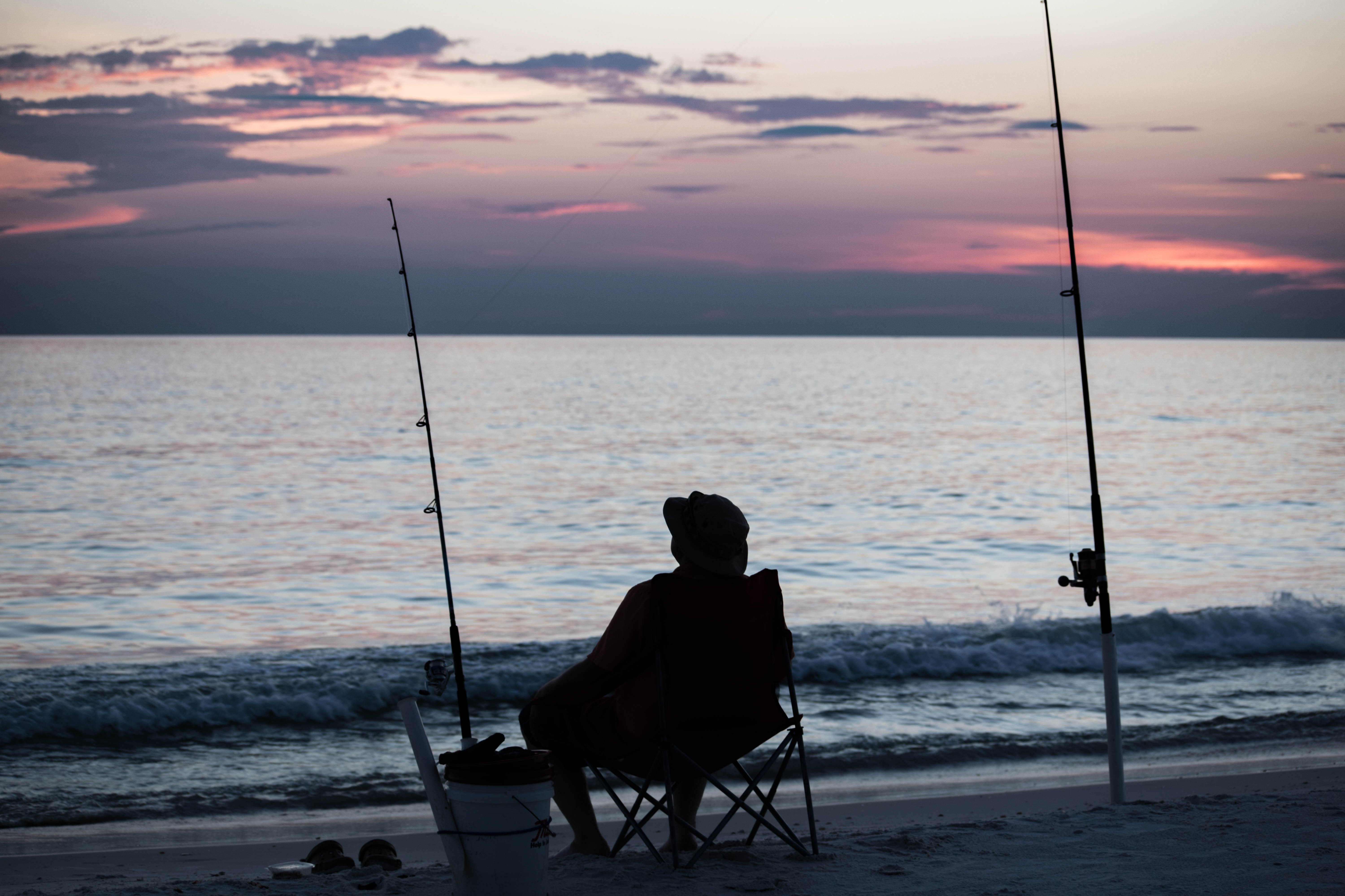 a person sitting in a chair on a beach with fishing poles