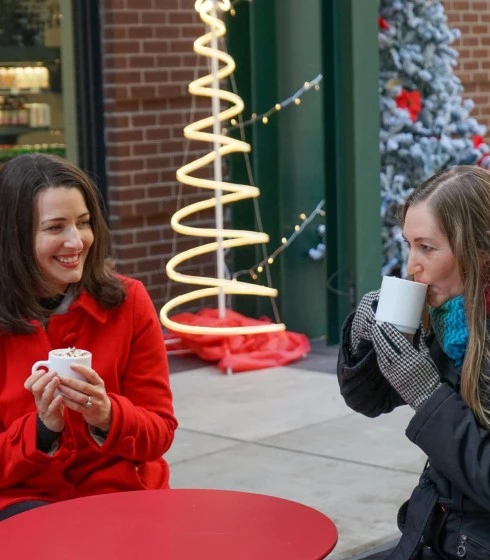 two women sitting outside drinking coffee