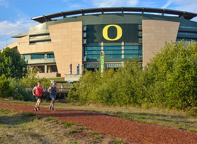 a man and woman running on a trail in front of a stadium