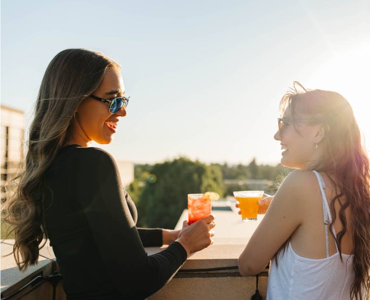 two women holding drinks on a balcony