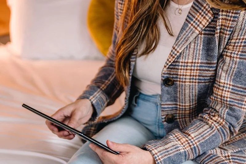 a woman sitting on a bed holding a tablet
