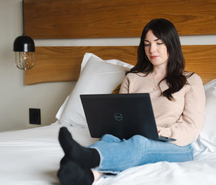 a woman sitting on a bed using a laptop