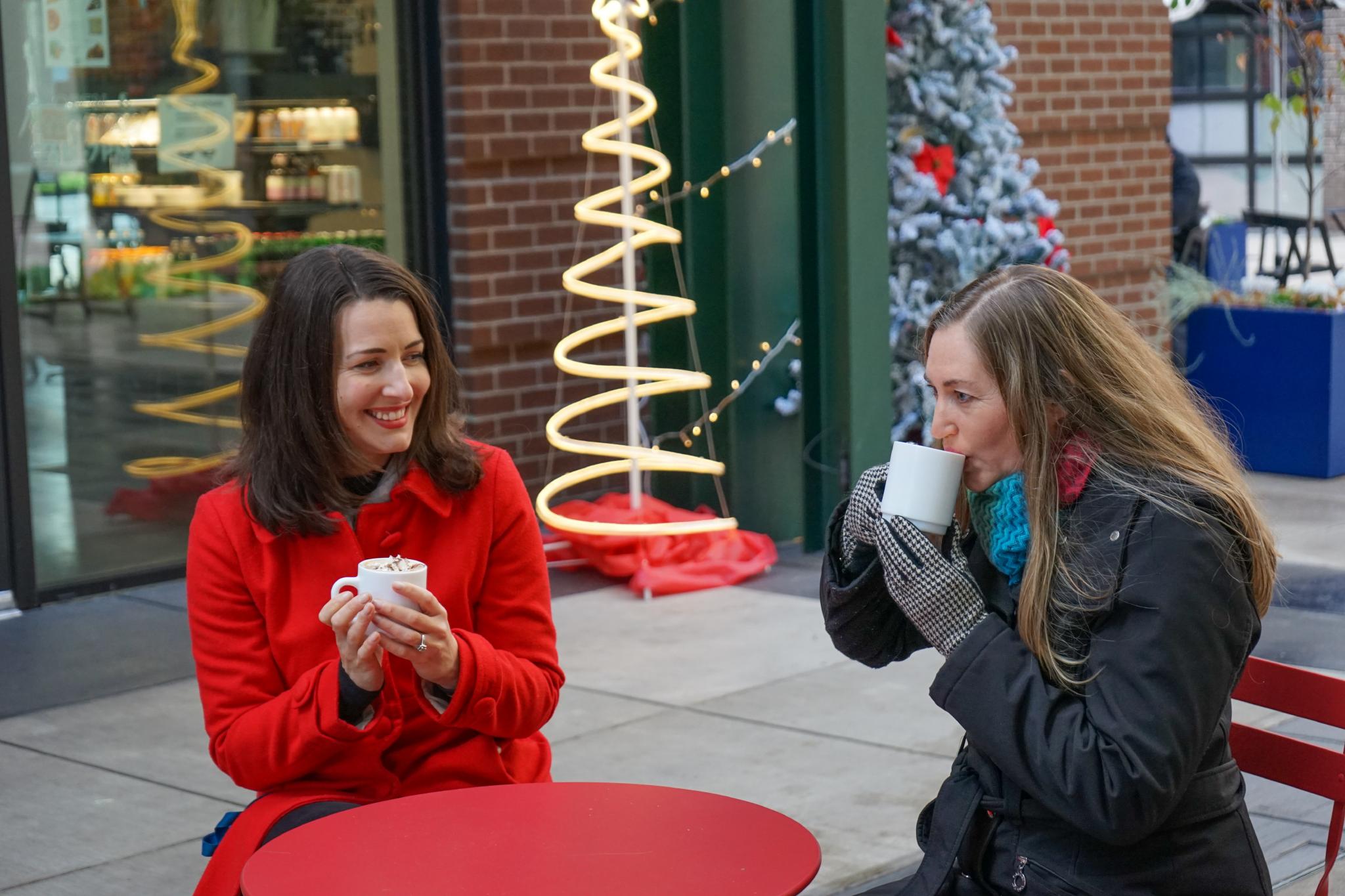 two women sitting outside drinking coffee