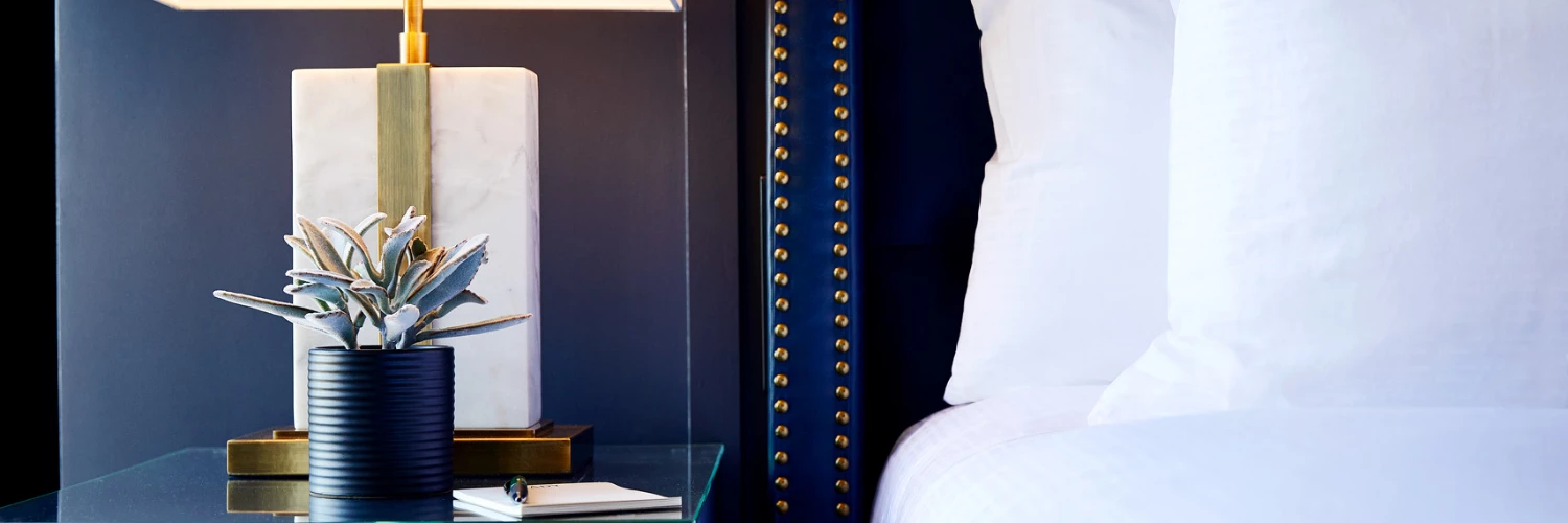 closeup shot of bed and bed side table with a plant and a gold and marble lamp