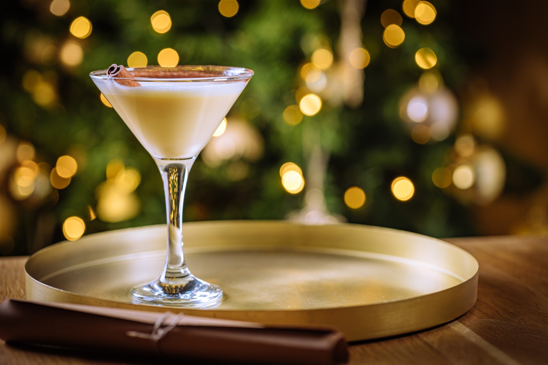 a glass of white liquid with cinnamon on top of a gold tray