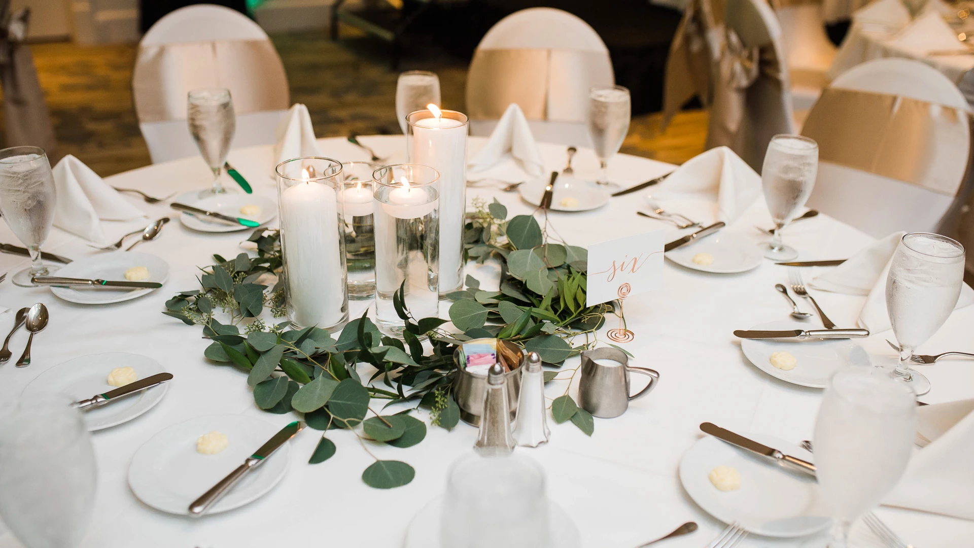 a table set with white plates and candles