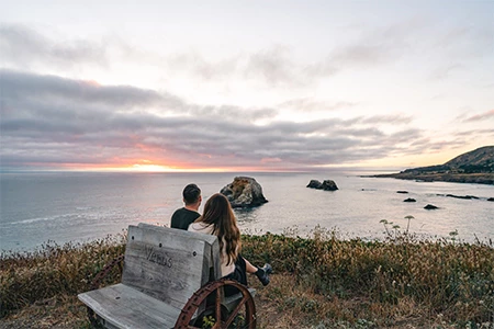 a man and woman sitting on a bench overlooking a body of water