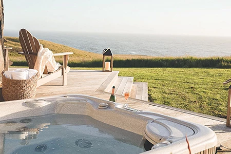 a woman sitting on a deck with a hot tub and a bottle of wine