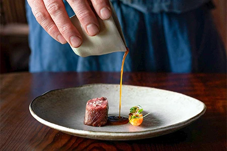 a person pouring sauce on a plate